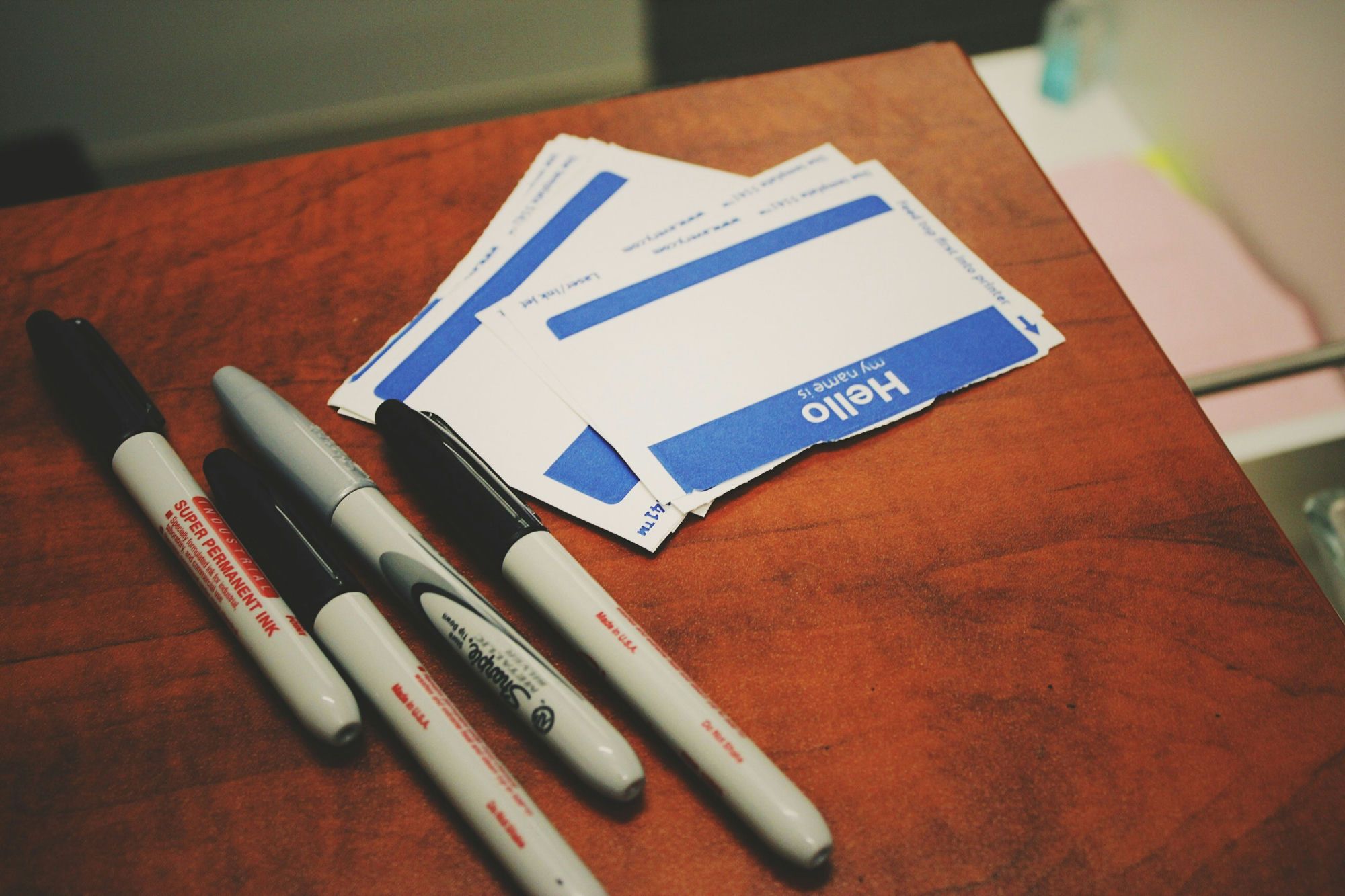 "Hello my name is" name-tag stickers and Sharpie markers on a desk. Photo by Jon Tyson on Unsplash.